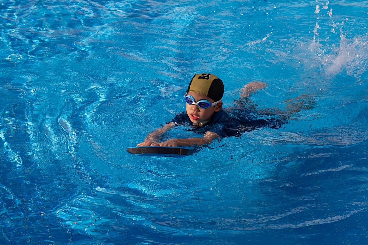 Kind mit Schwimmbrille und Schwimmbrett übt im Wasser das Schwimmenlernen.
